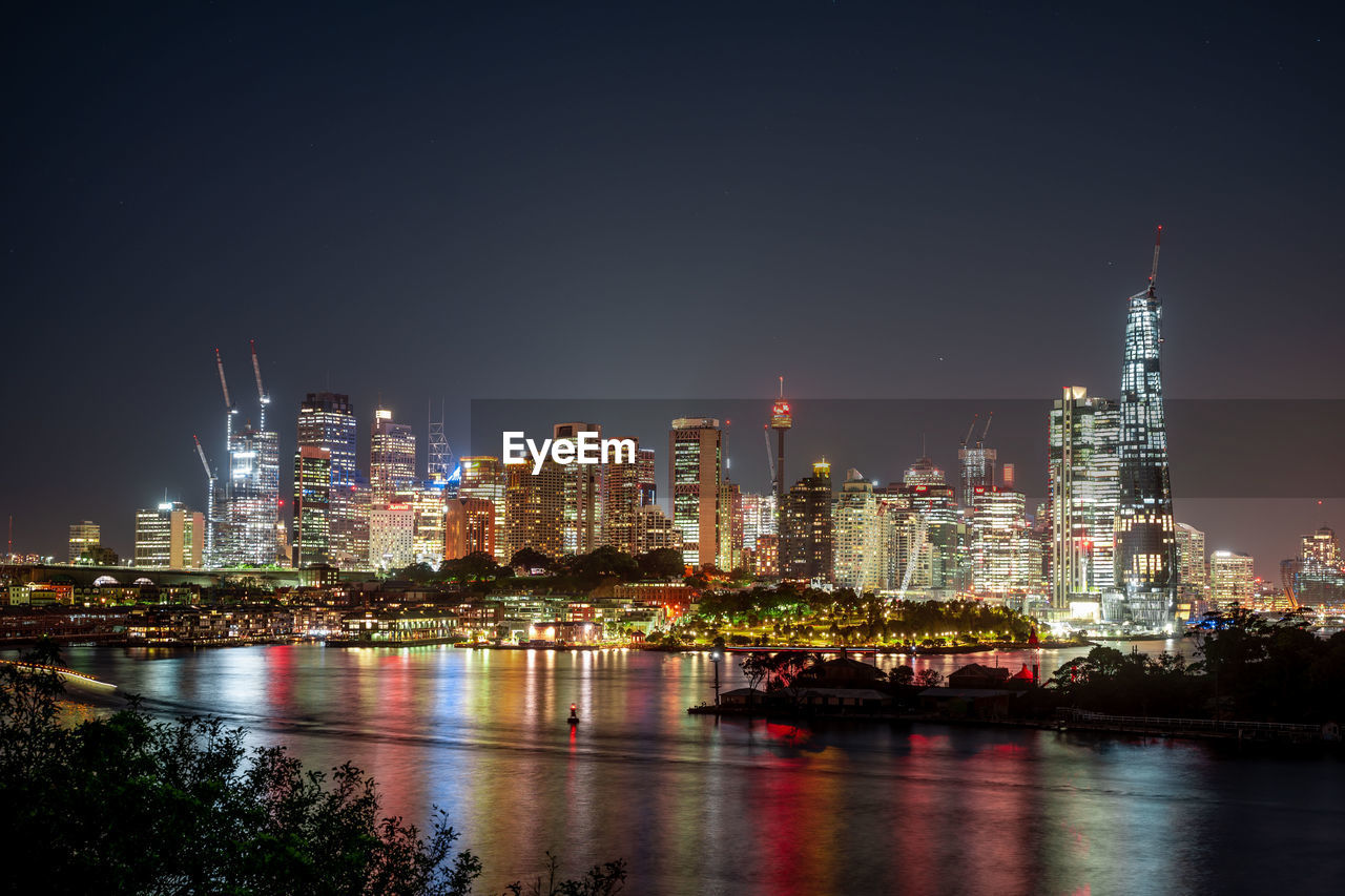 ILLUMINATED BUILDINGS BY RIVER AGAINST SKY