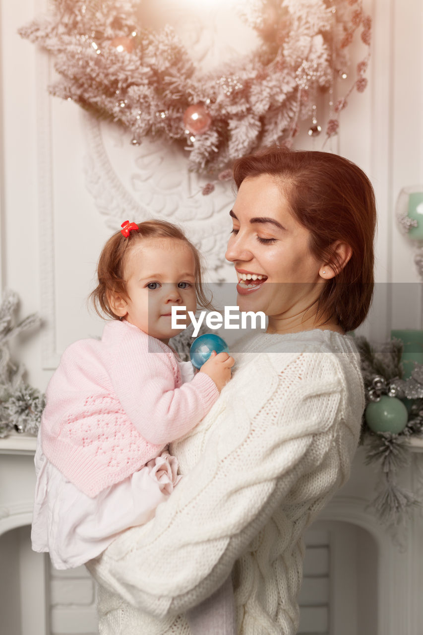 Cheerful mother carrying daughter during christmas at home