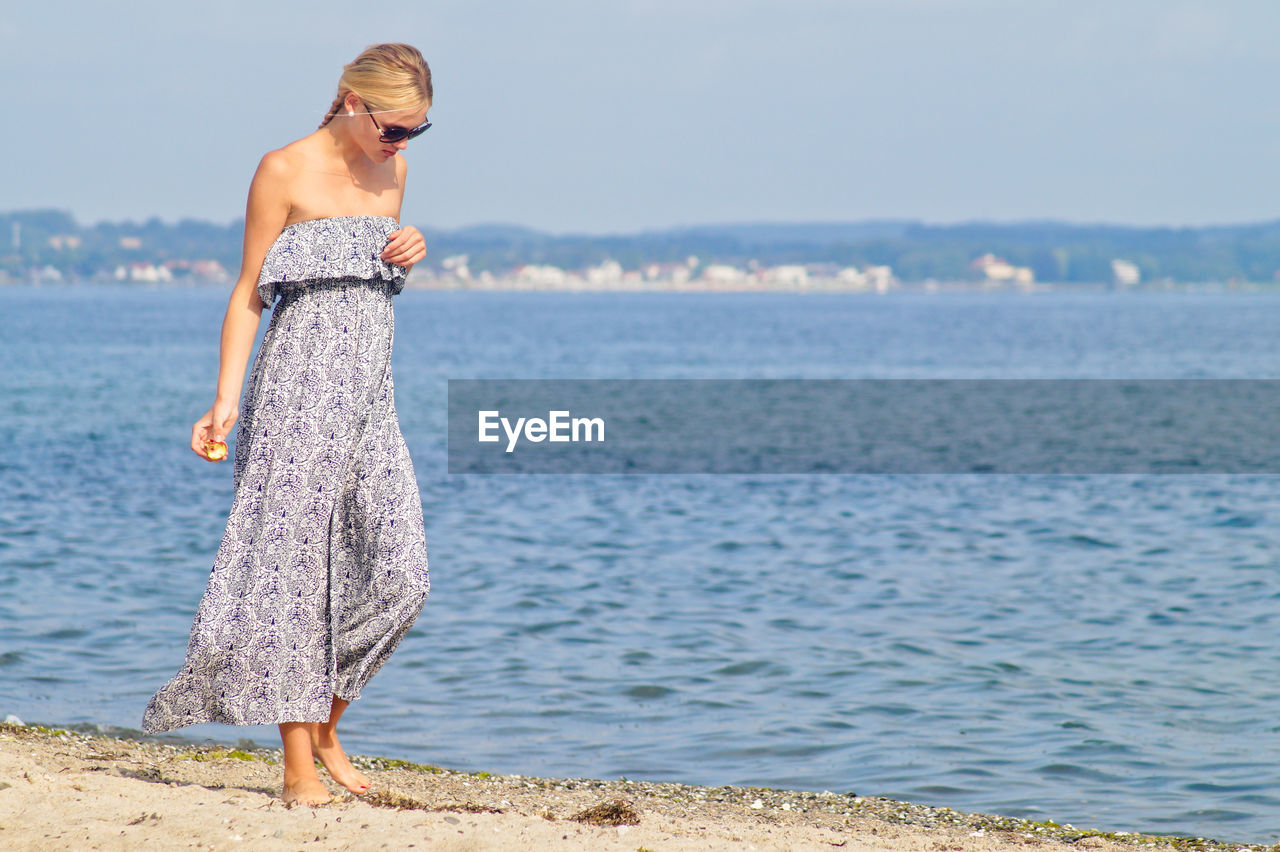 Woman walking on shore at beach against sky