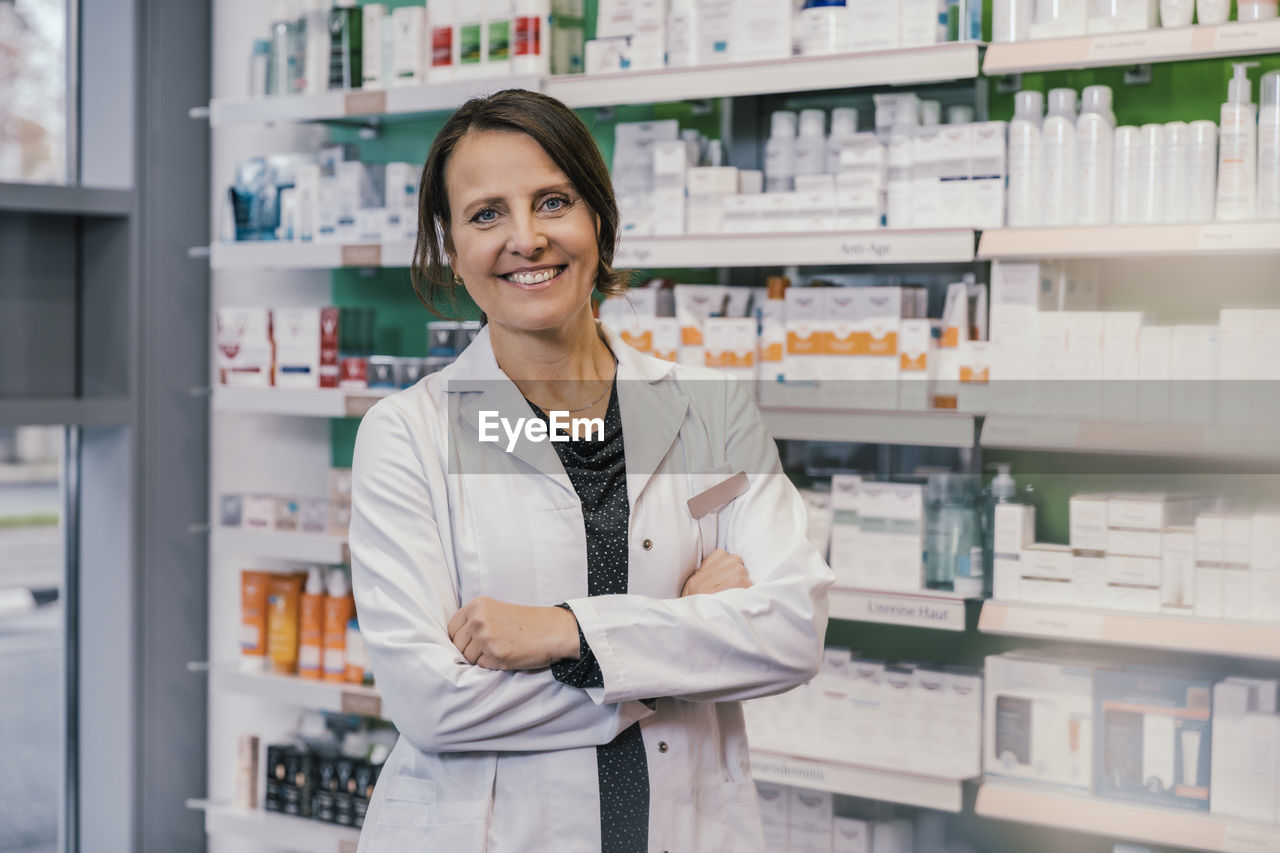 Confident female pharmacist with arms crossed in chemist shop