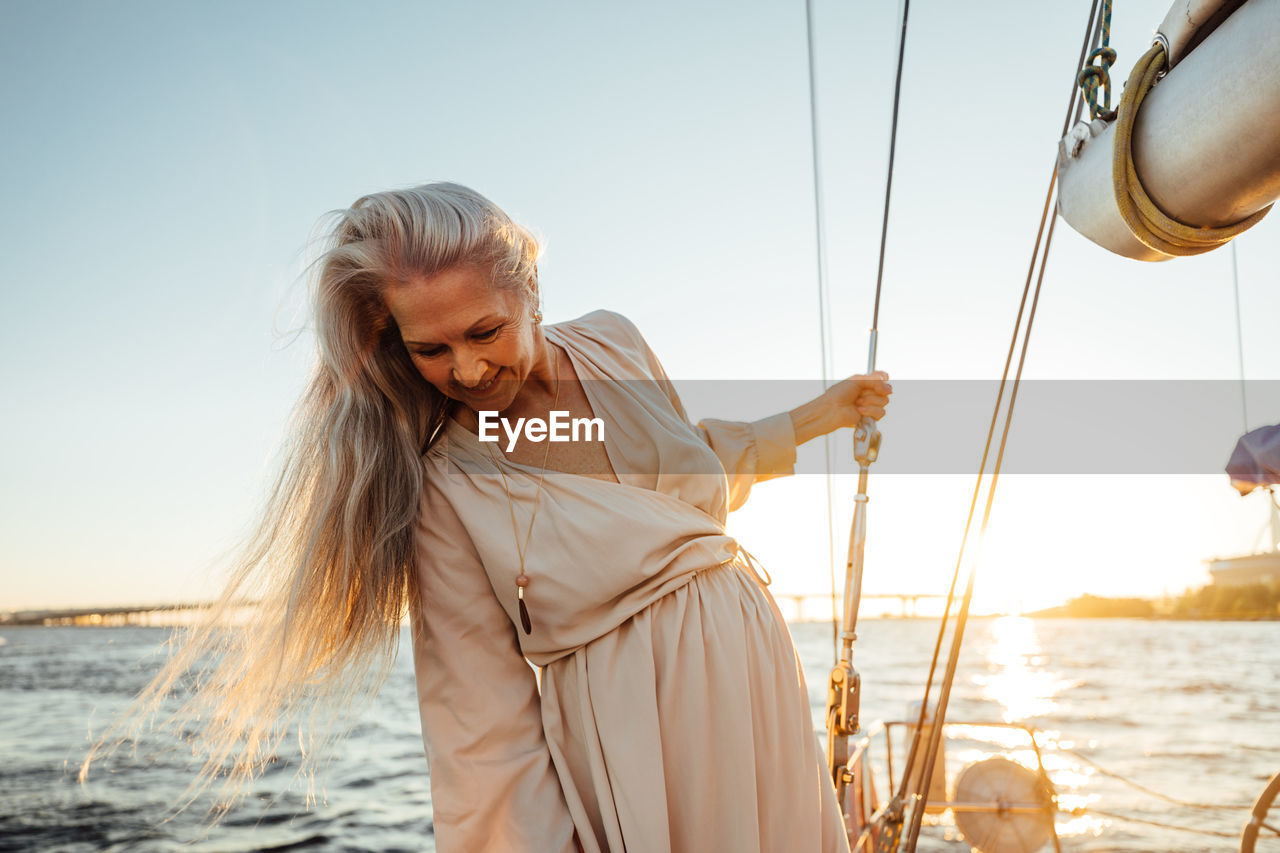 Beautiful senior woman in boat sailing on sea against sky