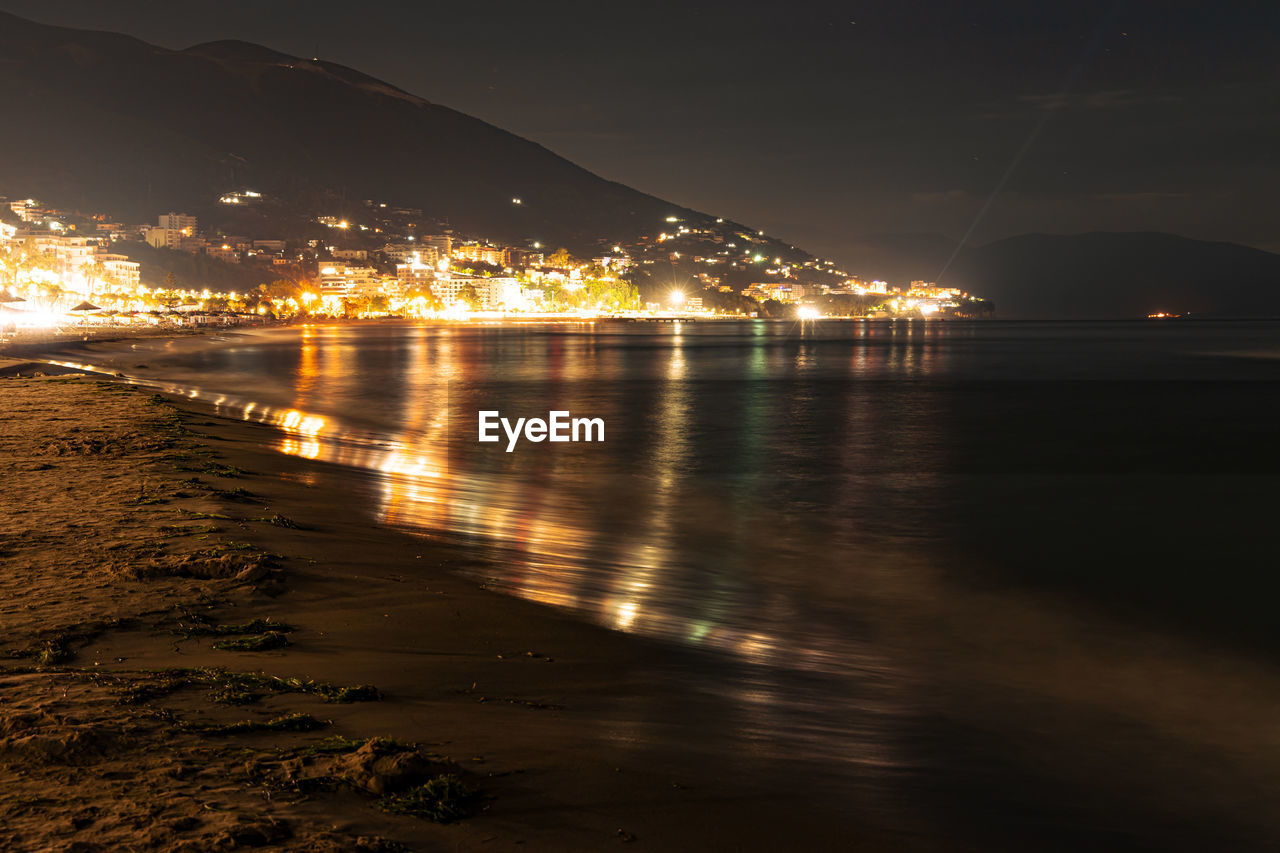 SCENIC VIEW OF ILLUMINATED CITY BY SEA AGAINST SKY