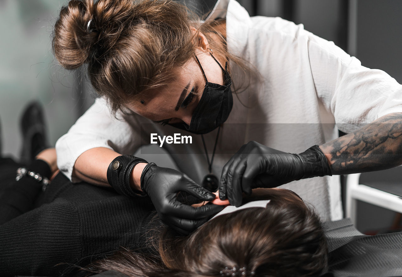 Woman piercing female customer ear in studio
