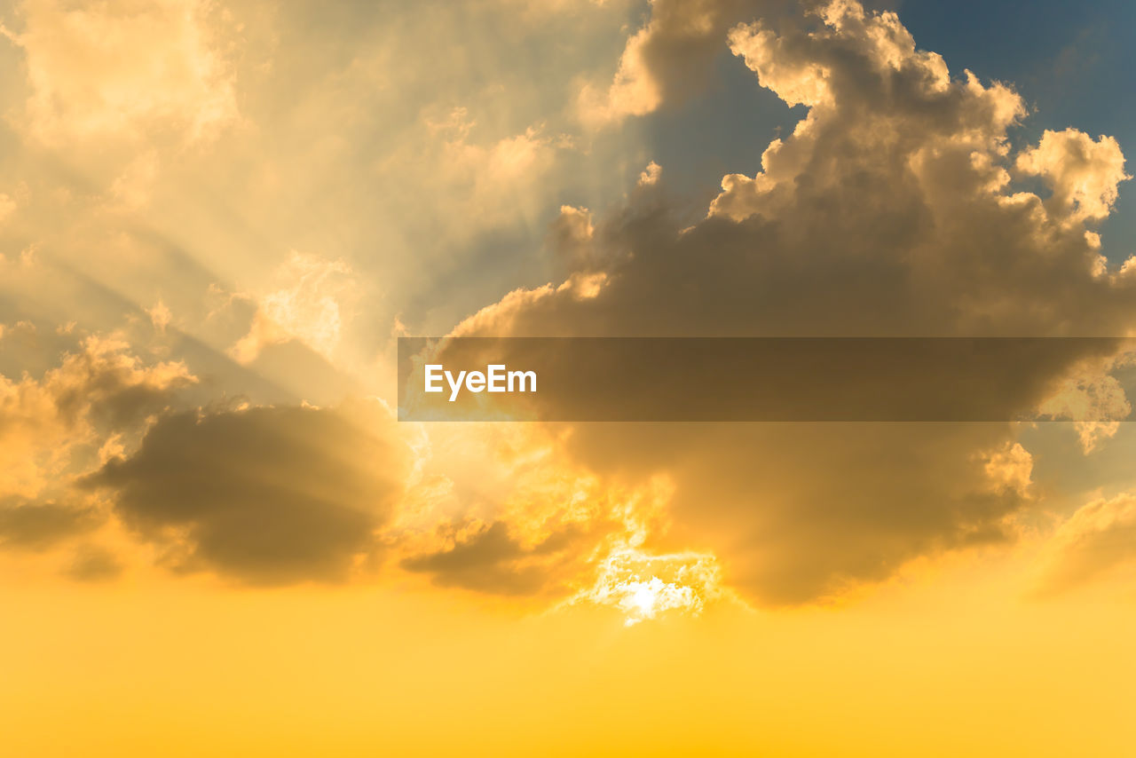 Low angle view of sunlight streaming through clouds during sunset