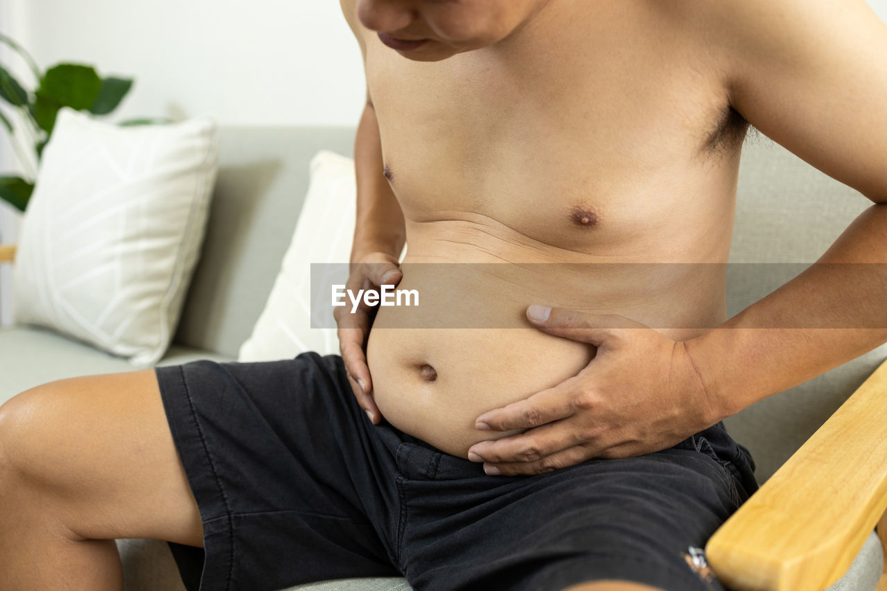 MIDSECTION OF SHIRTLESS MAN TOUCHING WOMAN SITTING ON SOFA