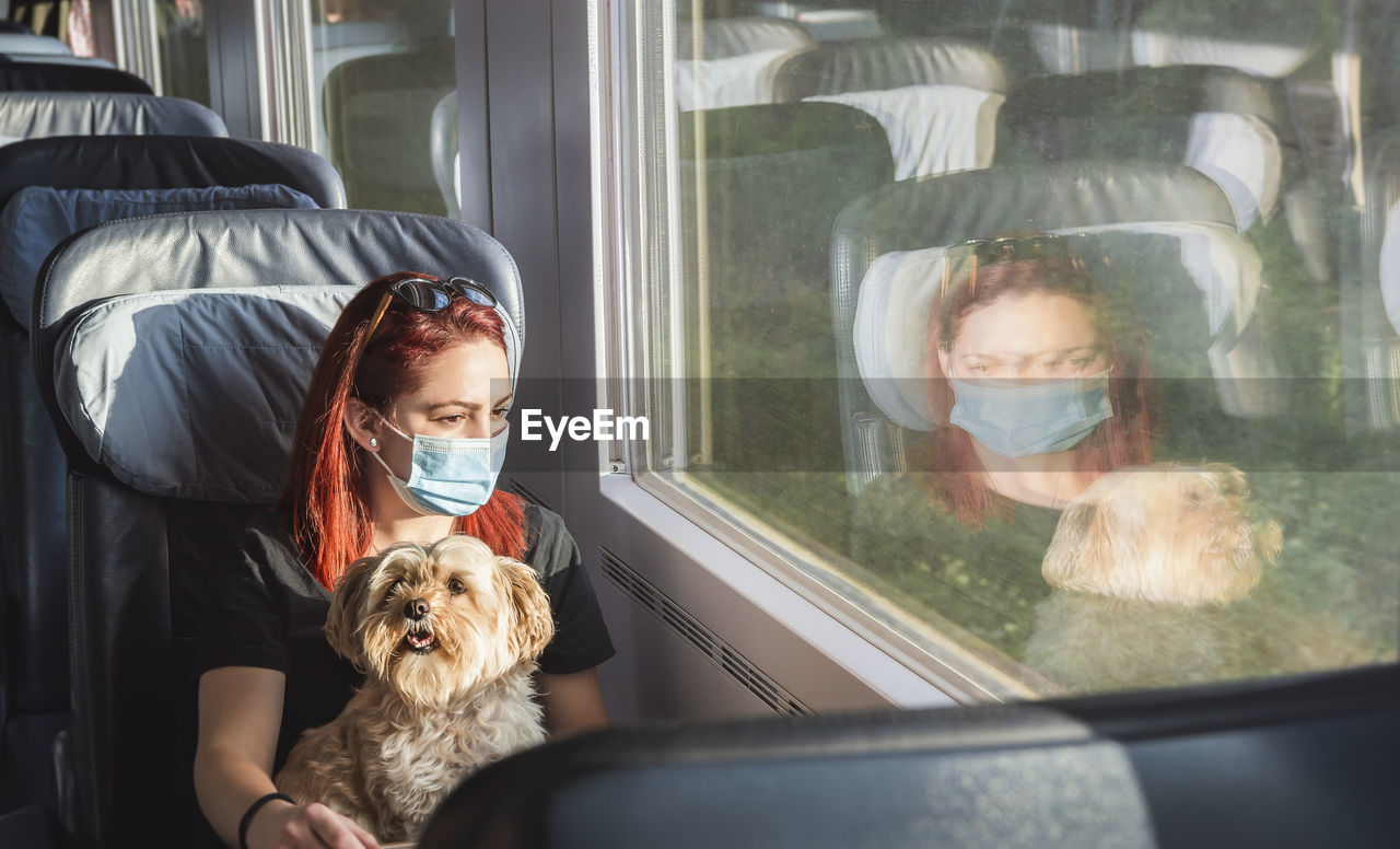 Young woman wearing mask sitting with dog in train