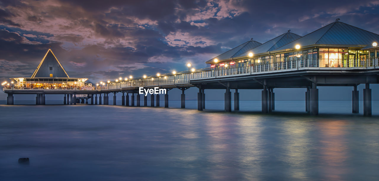 Illuminated bridge over sea against sky at night