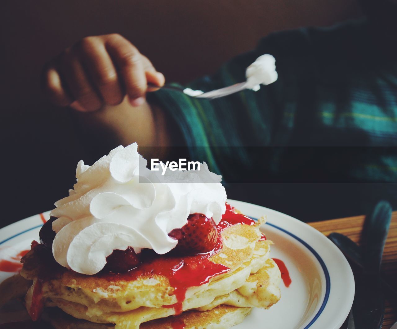 Midsection of child holding fork over pancake on table