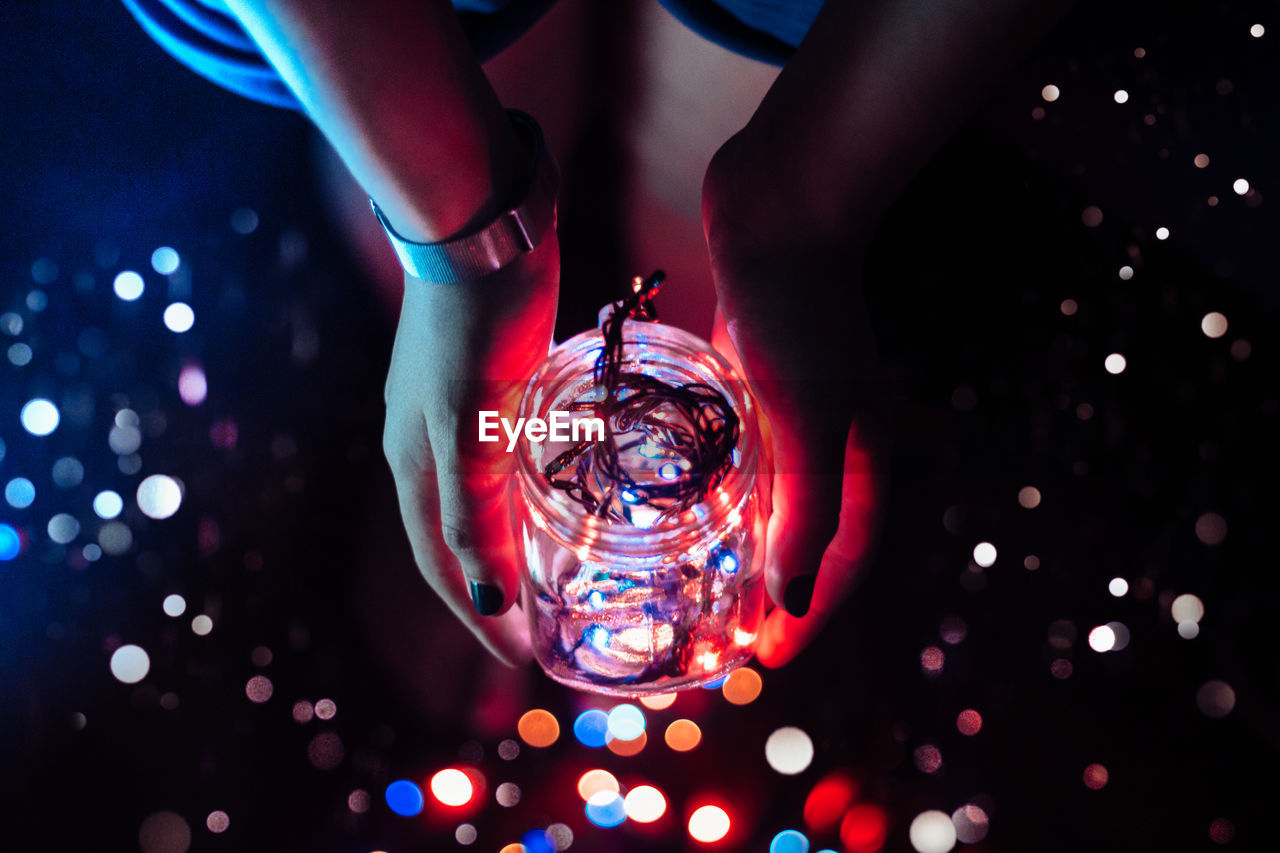 Low section of woman holding illuminated lights in jar at darkroom