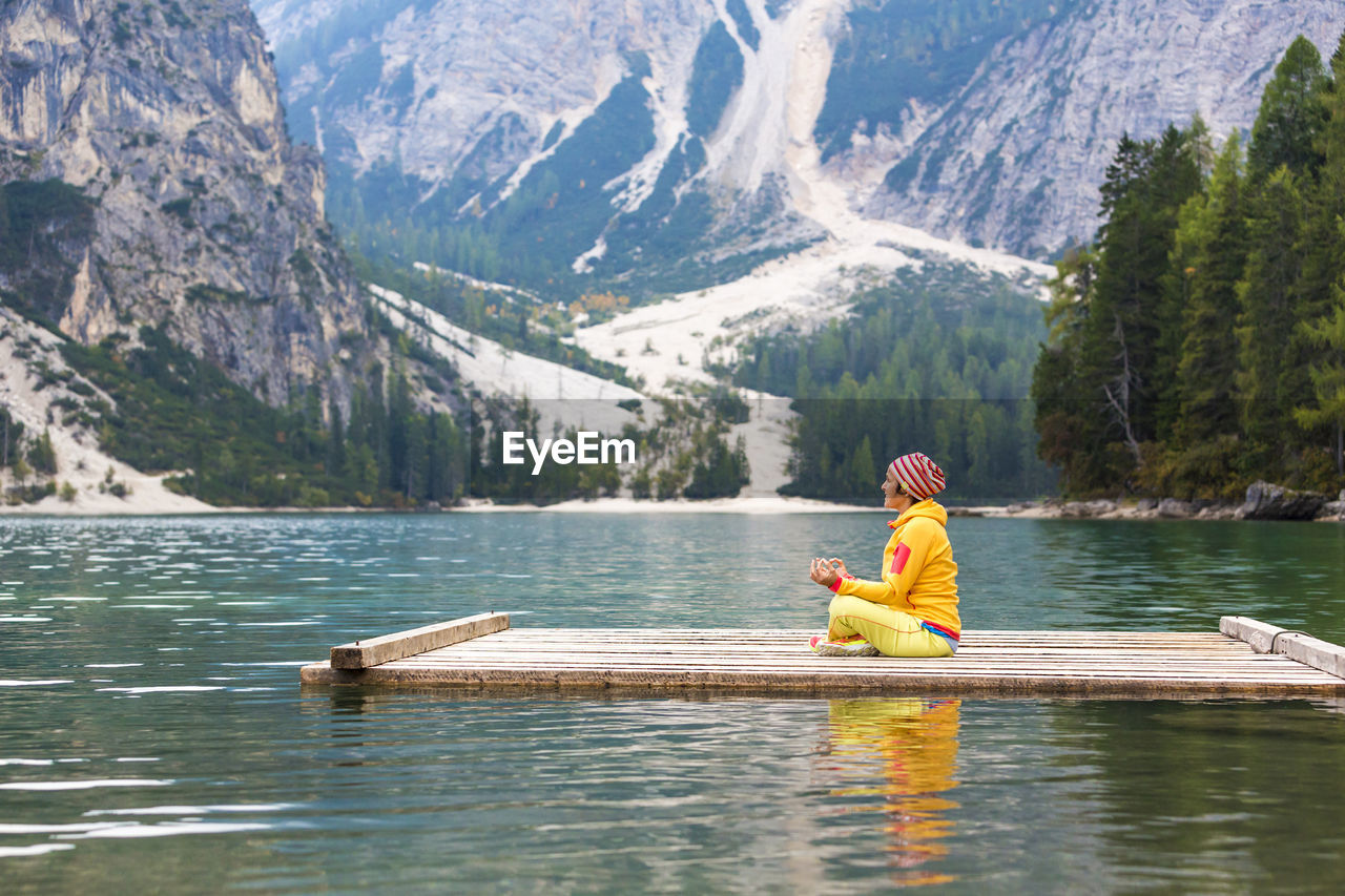 MAN SITTING ON LAKE AGAINST MOUNTAIN