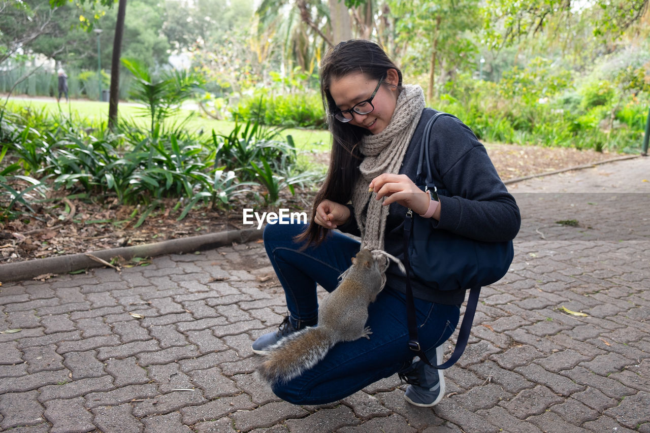 Portrait of squirrel climbing on a kneeling woman with scarf and handbag 