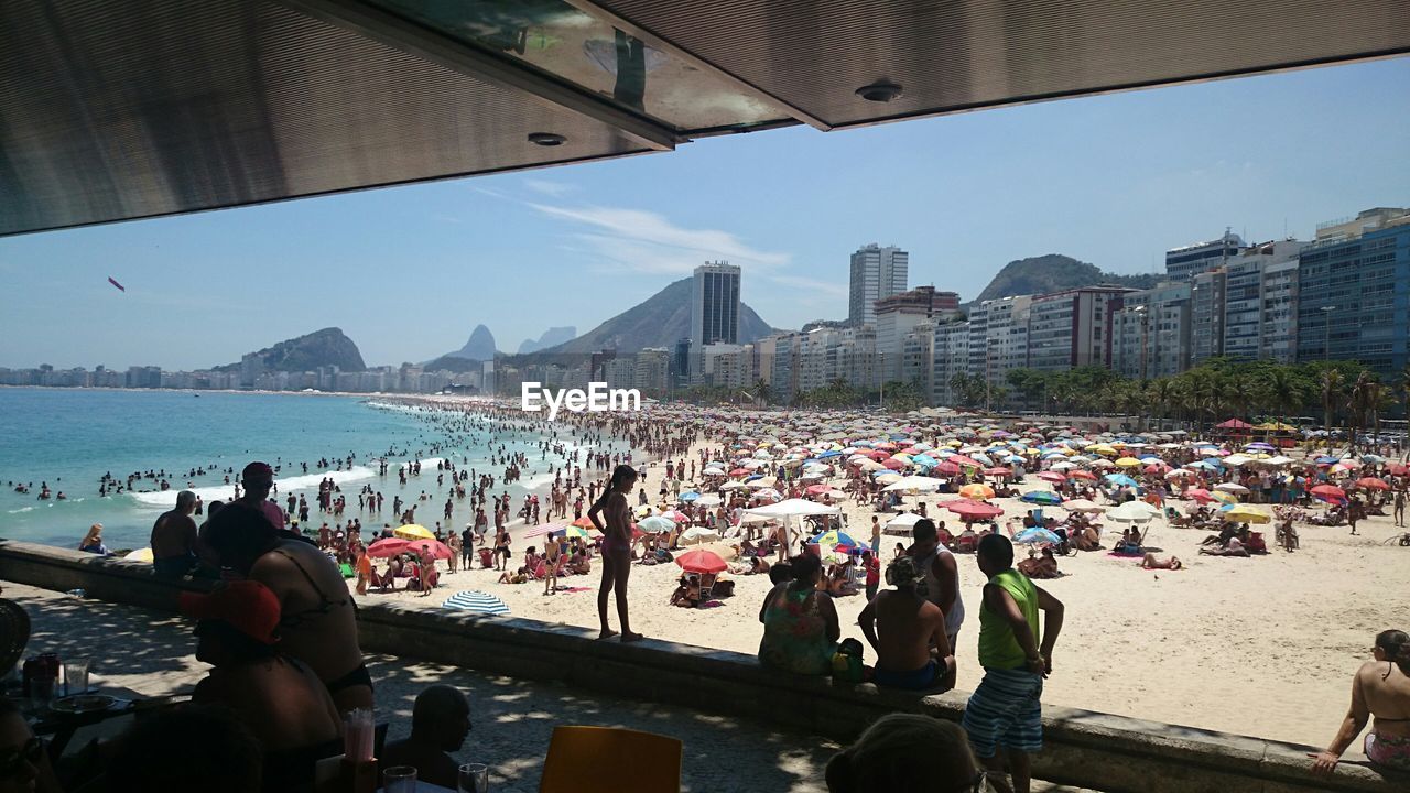 Scenic view of crowded beach by sea against buildings