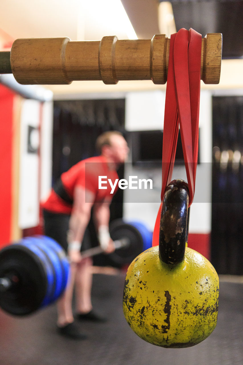 Kettlebell hanging on wood while man exercising in background
