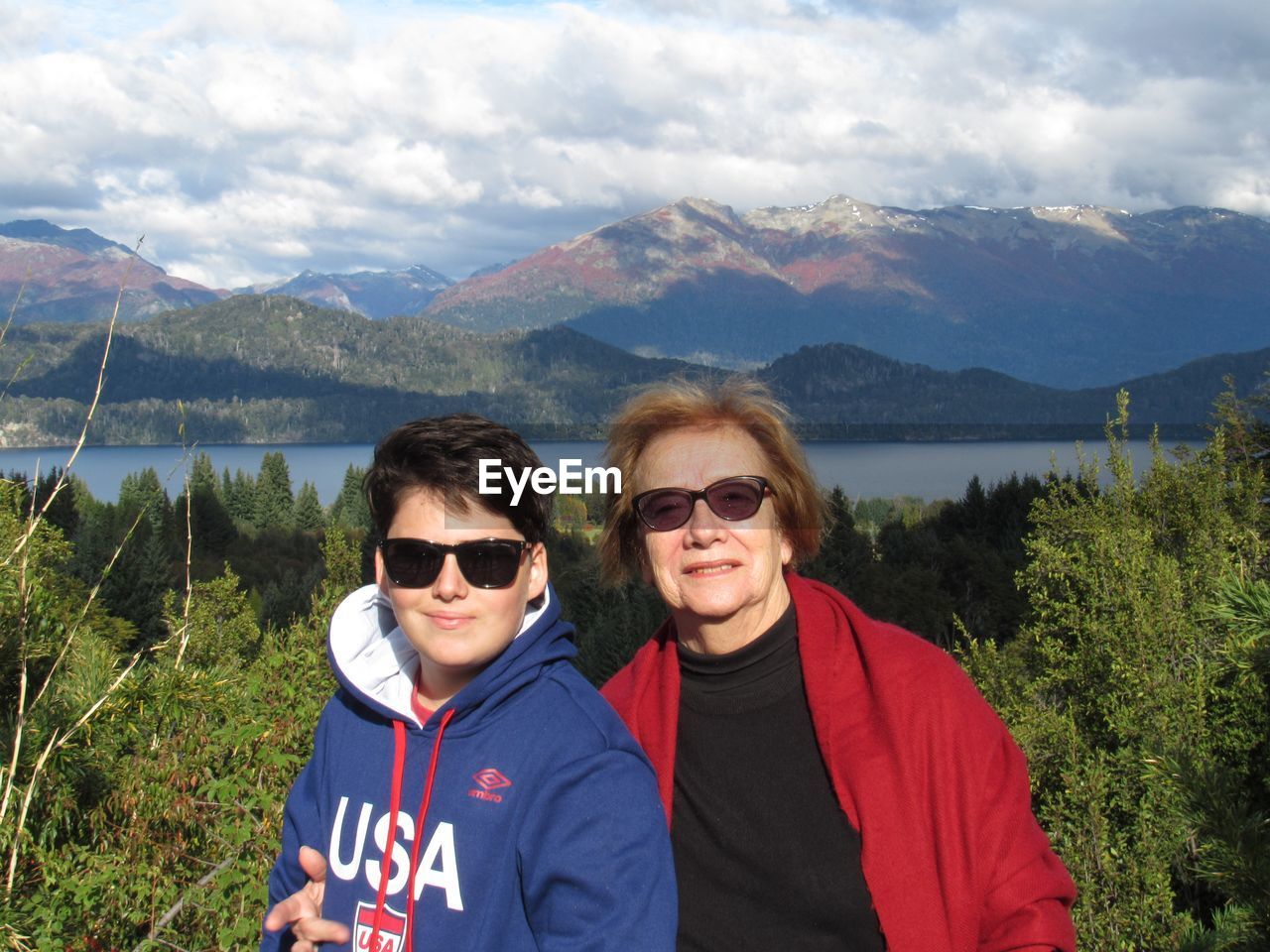 Portrait of mother and son standing at lakeshore against mountains