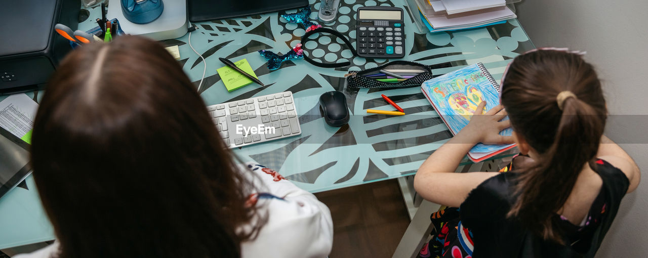 High angle view of mother and daughter sitting at desk