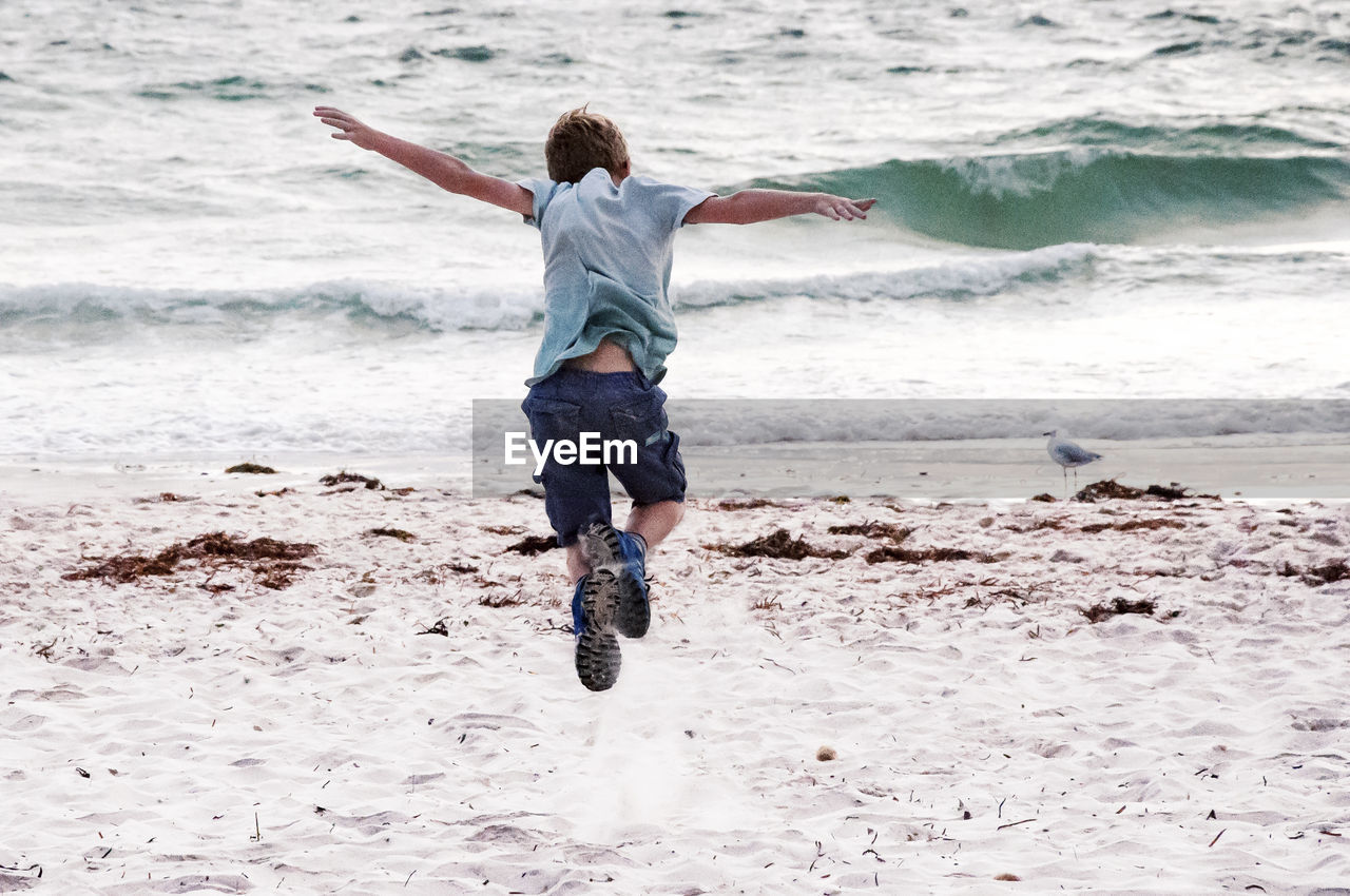Full length rear view of boy jumping on shore