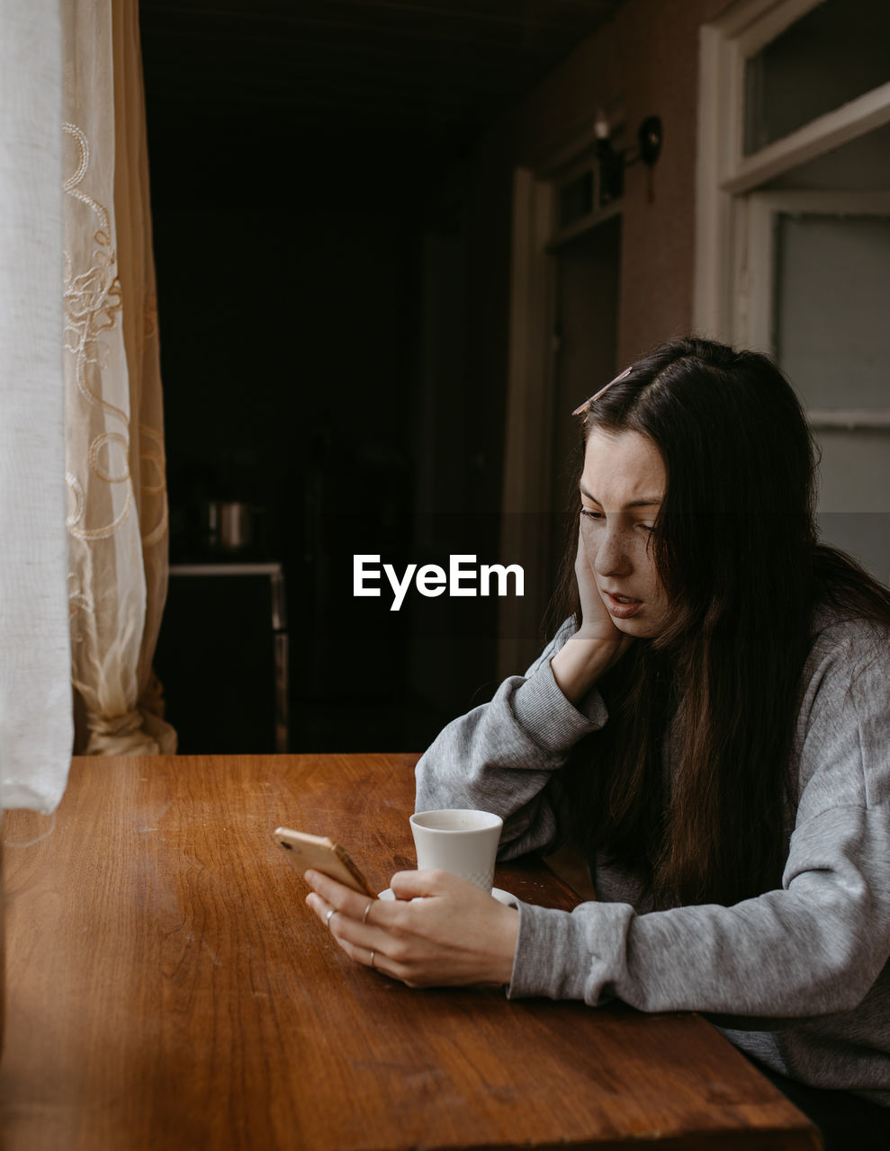 Freelance woman with the coffee and mobile phone at home talking expressiv