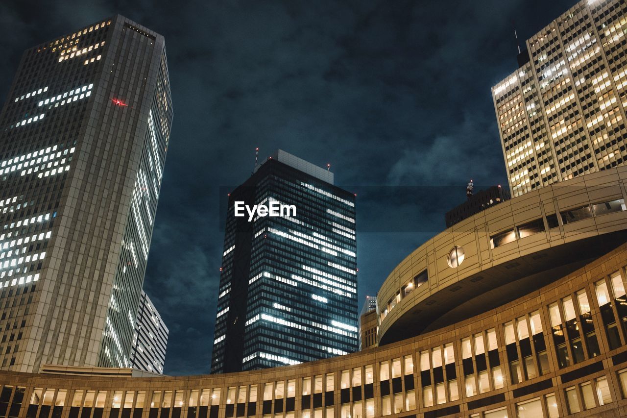 Low angle view of illuminated modern buildings against cloudy sky at night