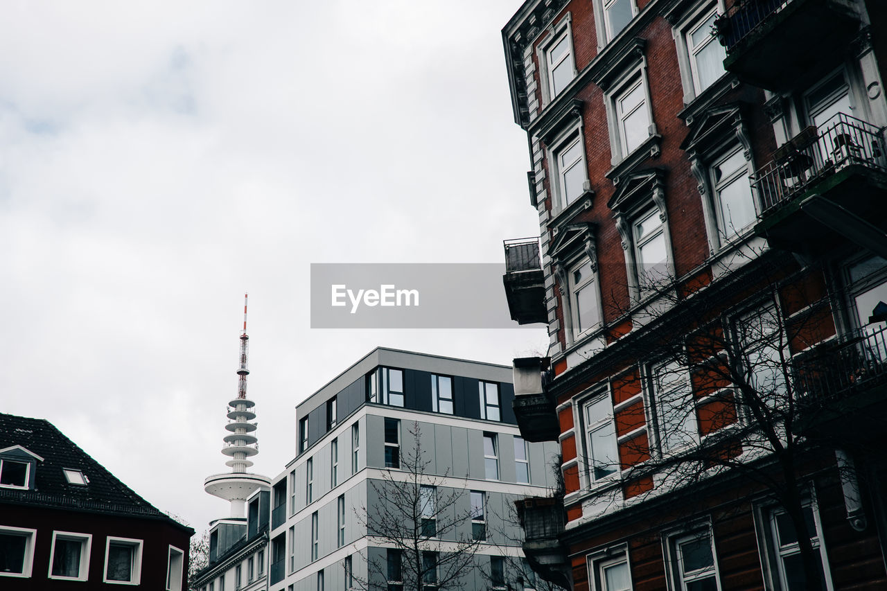 Low angle view of heinrich-hertz-turm and buildings against cloudy sky in city