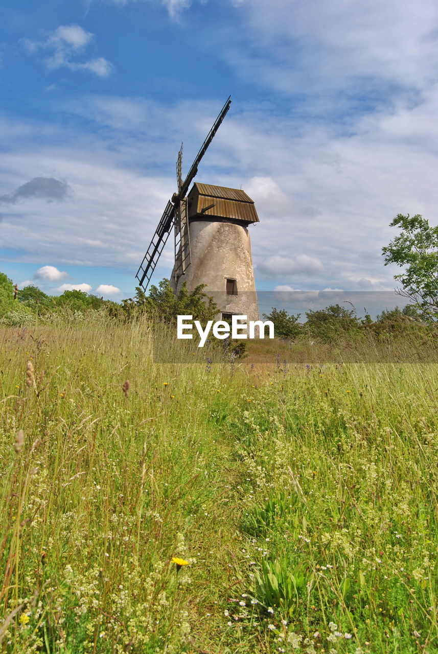 Low angle view of traditional windmill on grassy field against cloudy sky