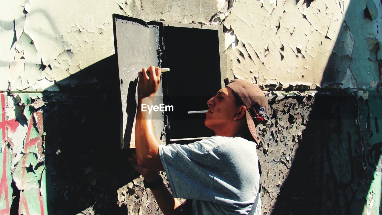 Young man writing on metallic door mounted over weathered wall