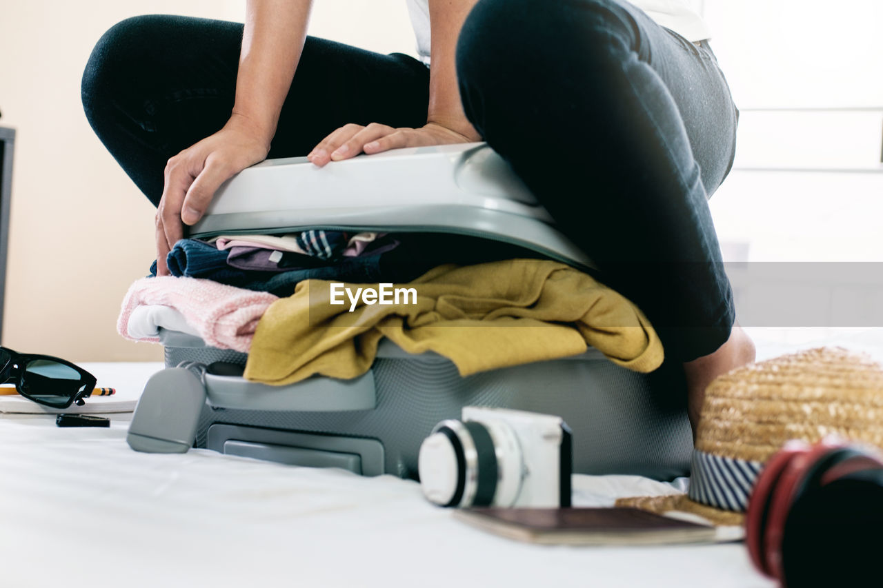 Midsection of woman packing overburdened clothes in suitcase 