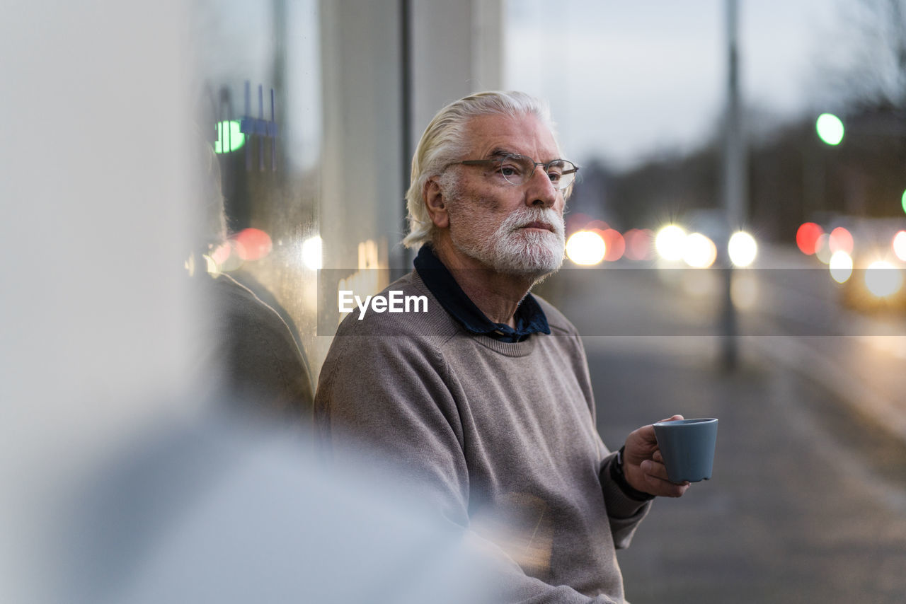 Senior man with eyeglasses holding coffee cup while sitting outside cafe