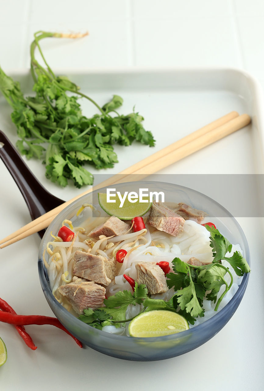 Pho bo, vietnamese fresh rice noodle soup with sliced beef, herbs, and chili.