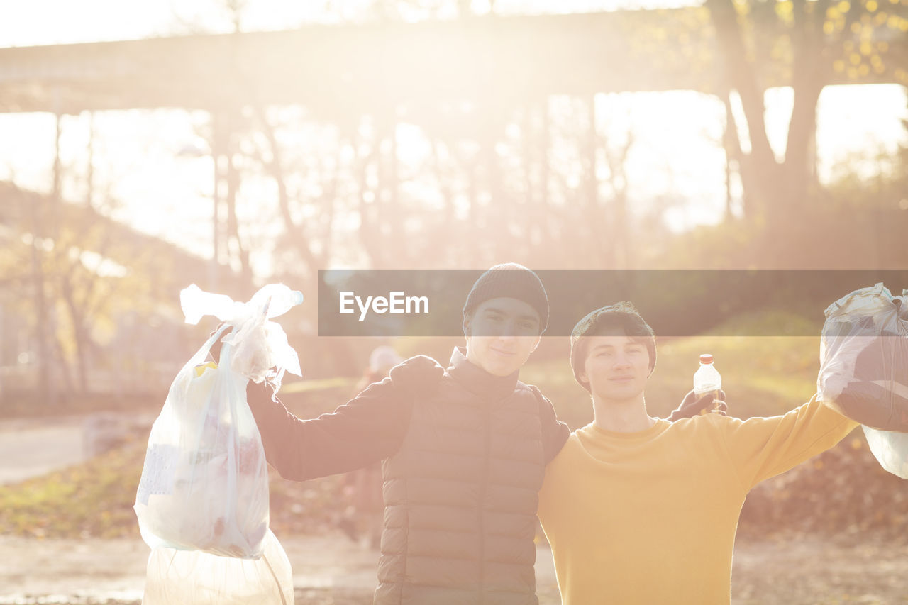 Portrait of young male volunteers with plastic garbage standing in public park