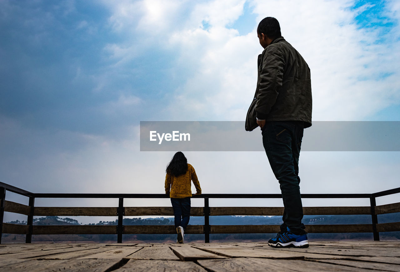 REAR VIEW OF MAN AND WOMAN STANDING ON RAILING