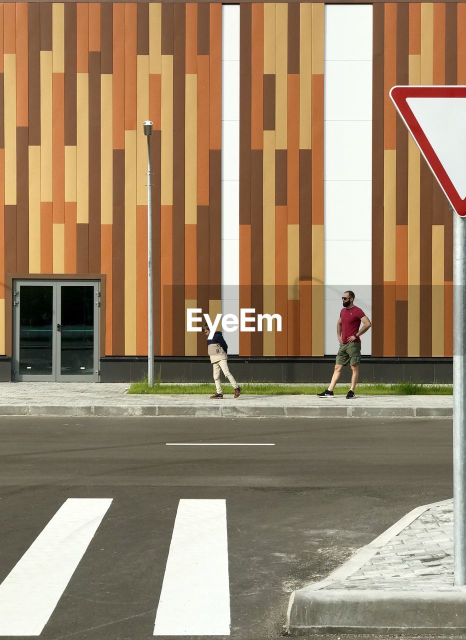 SIDE VIEW OF A MAN BICYCLING ON ROAD AGAINST BUILDING