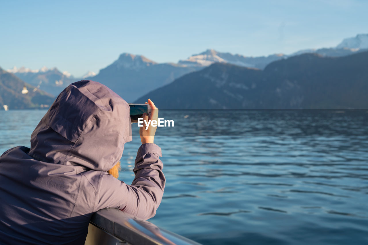 Close-up of woman photographing sea through mobile phone against mountain