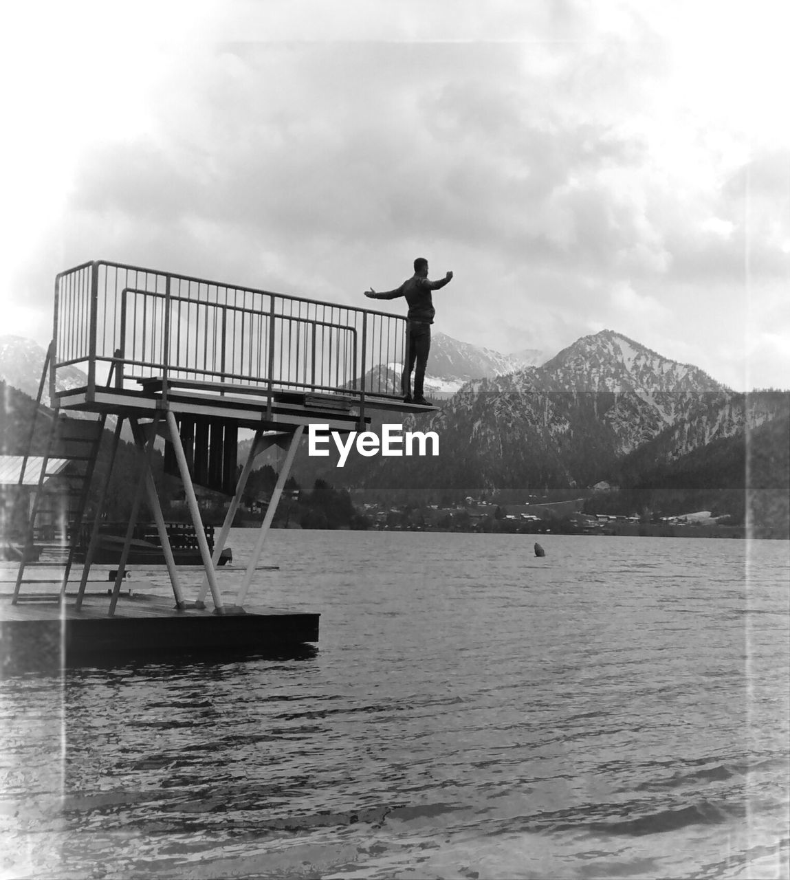 Man standing on pier by river with mountain in background