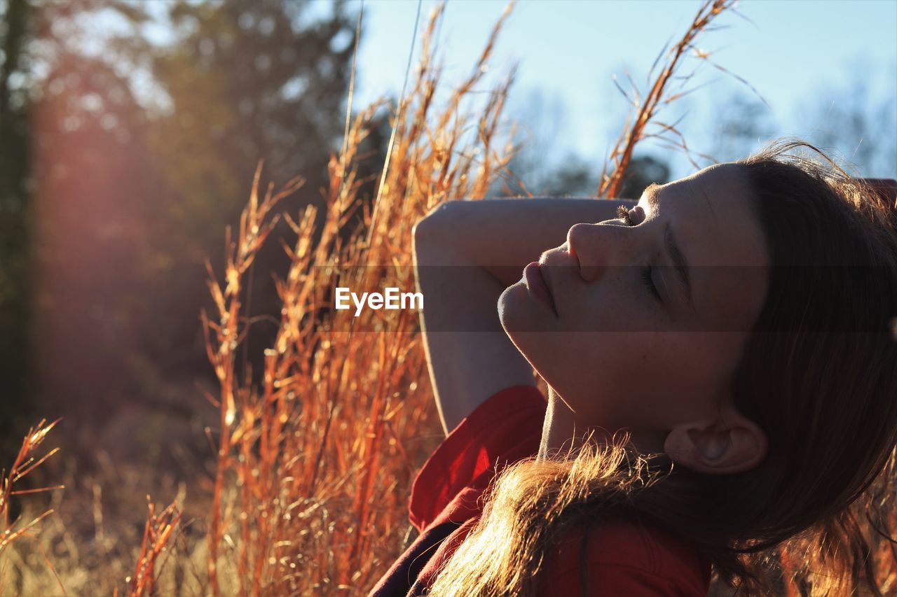 Thoughtful woman with head back and eyes closed sitting by plants during sunny day