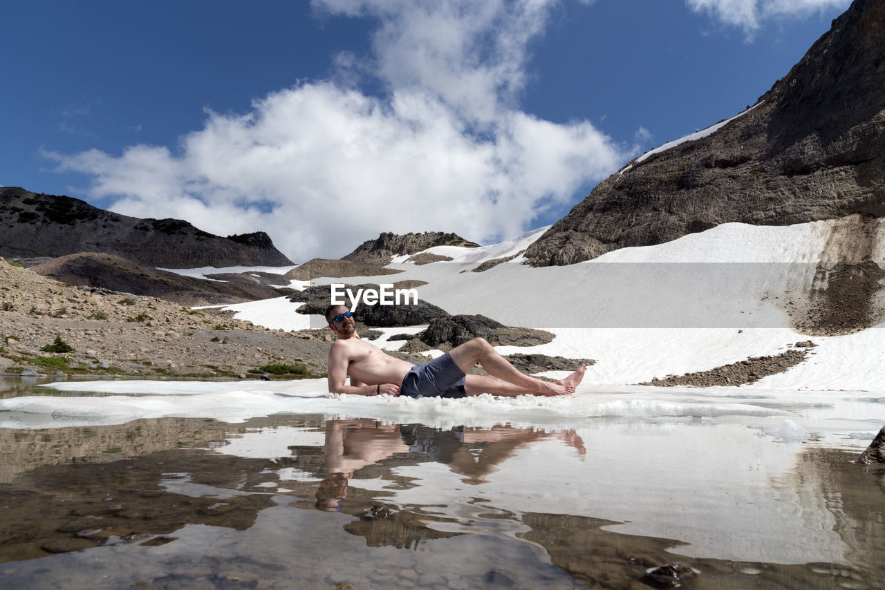 Man lying in lake against mountains during winter