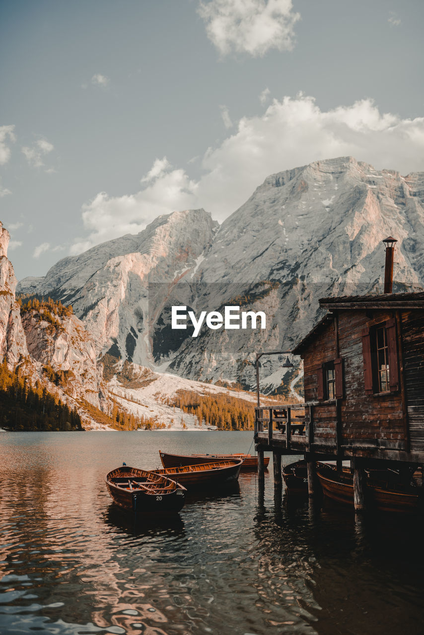 Stilt house with boats moored in lake against snowcapped mountains