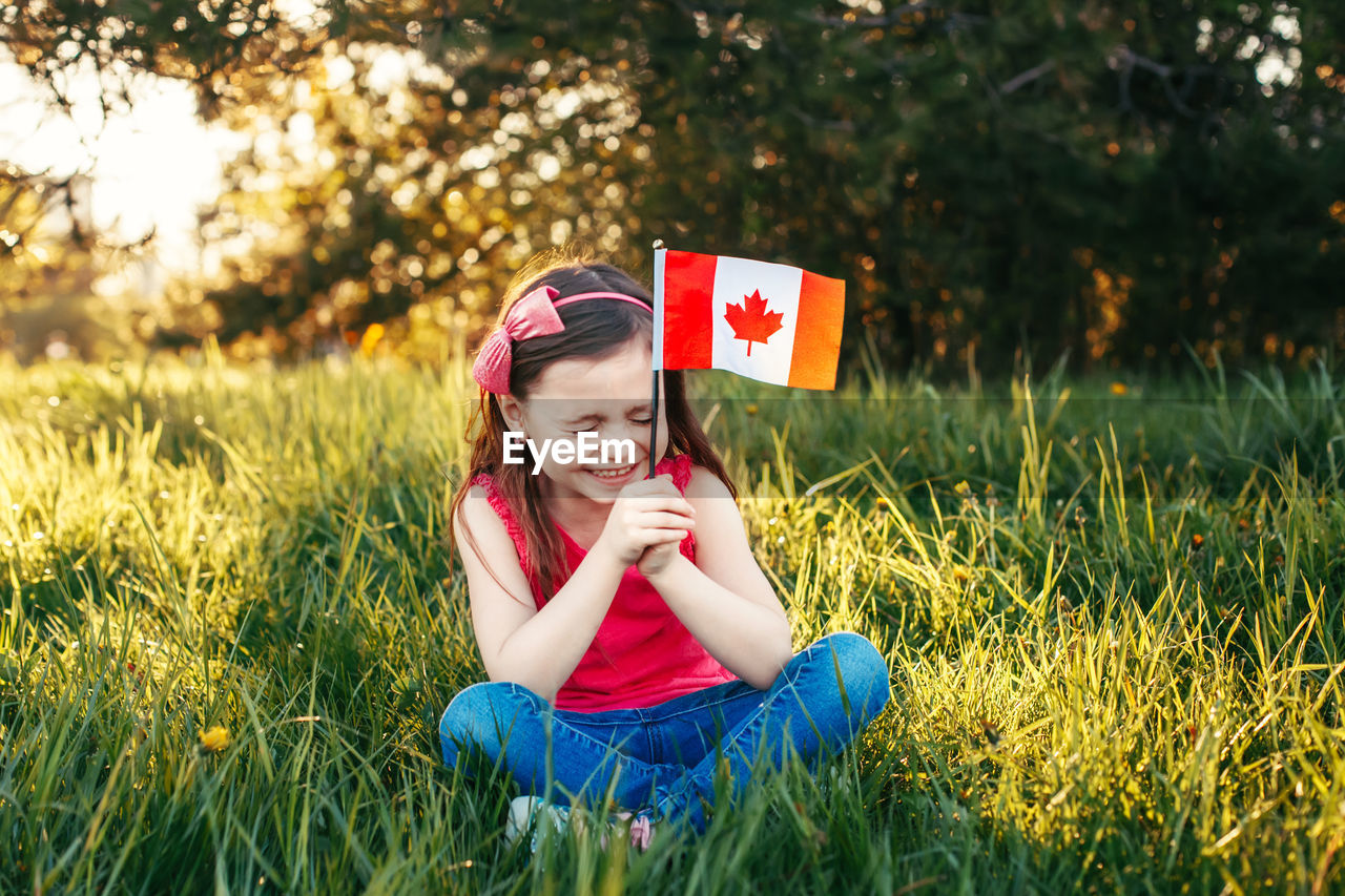 Happy girl with canadian flag sitting on field