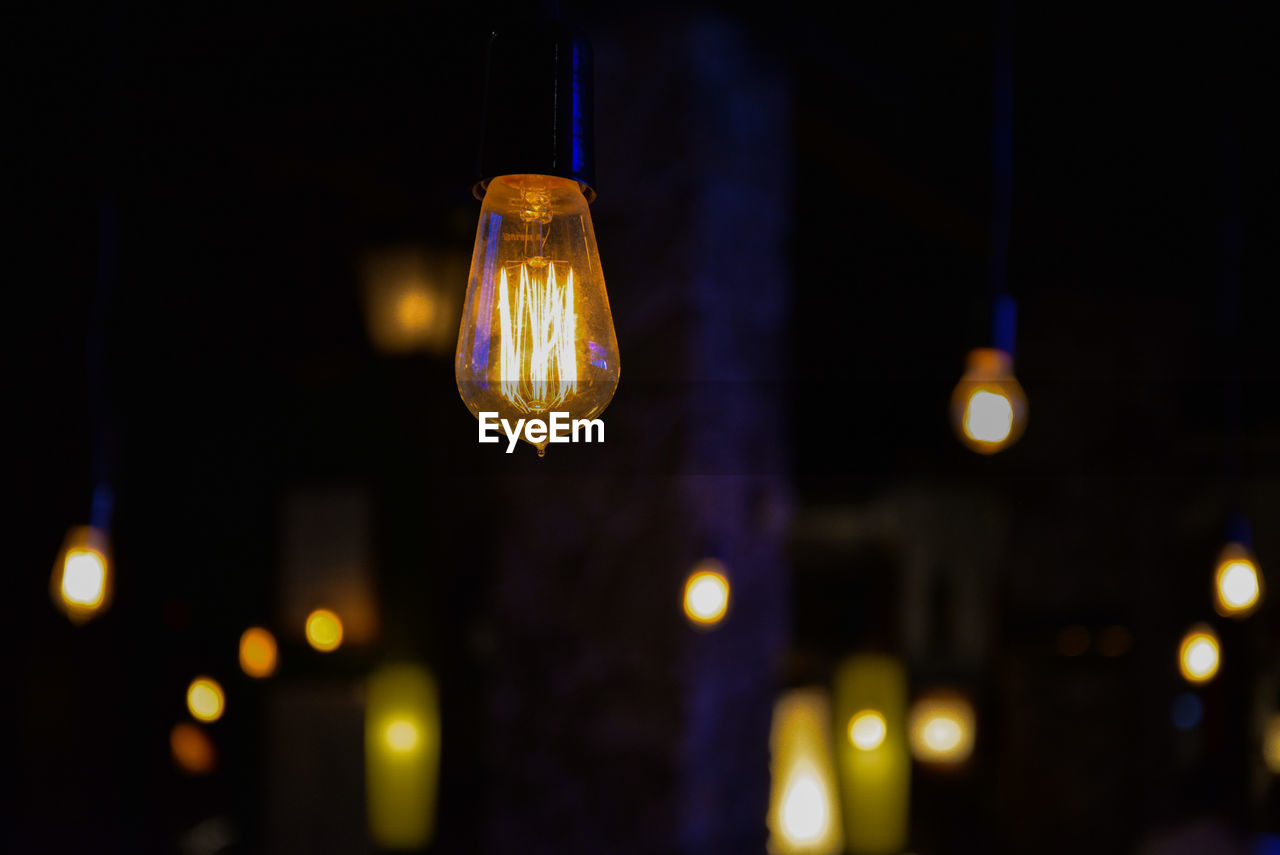 Low angle view of illuminated light bulb hanging at night