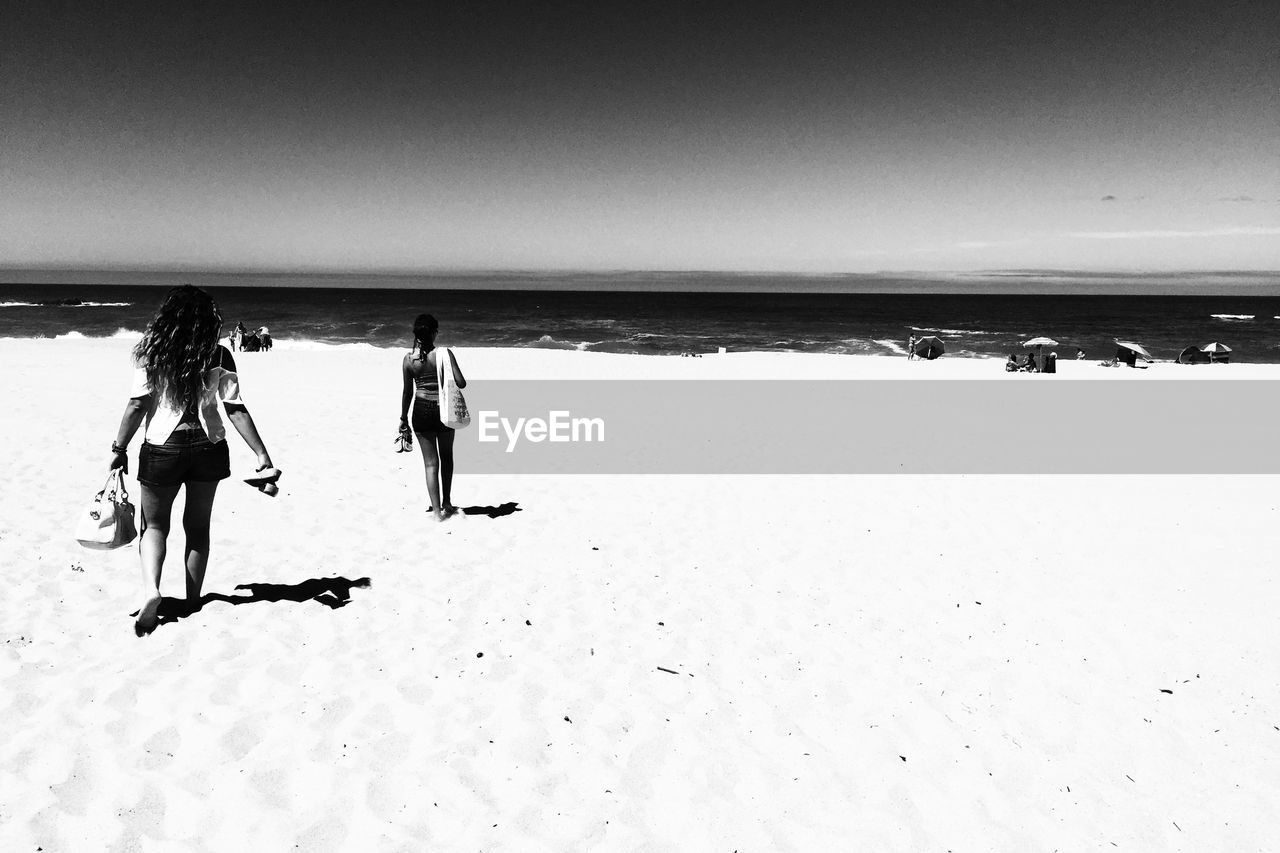 Rear view of women walking on beach during summer