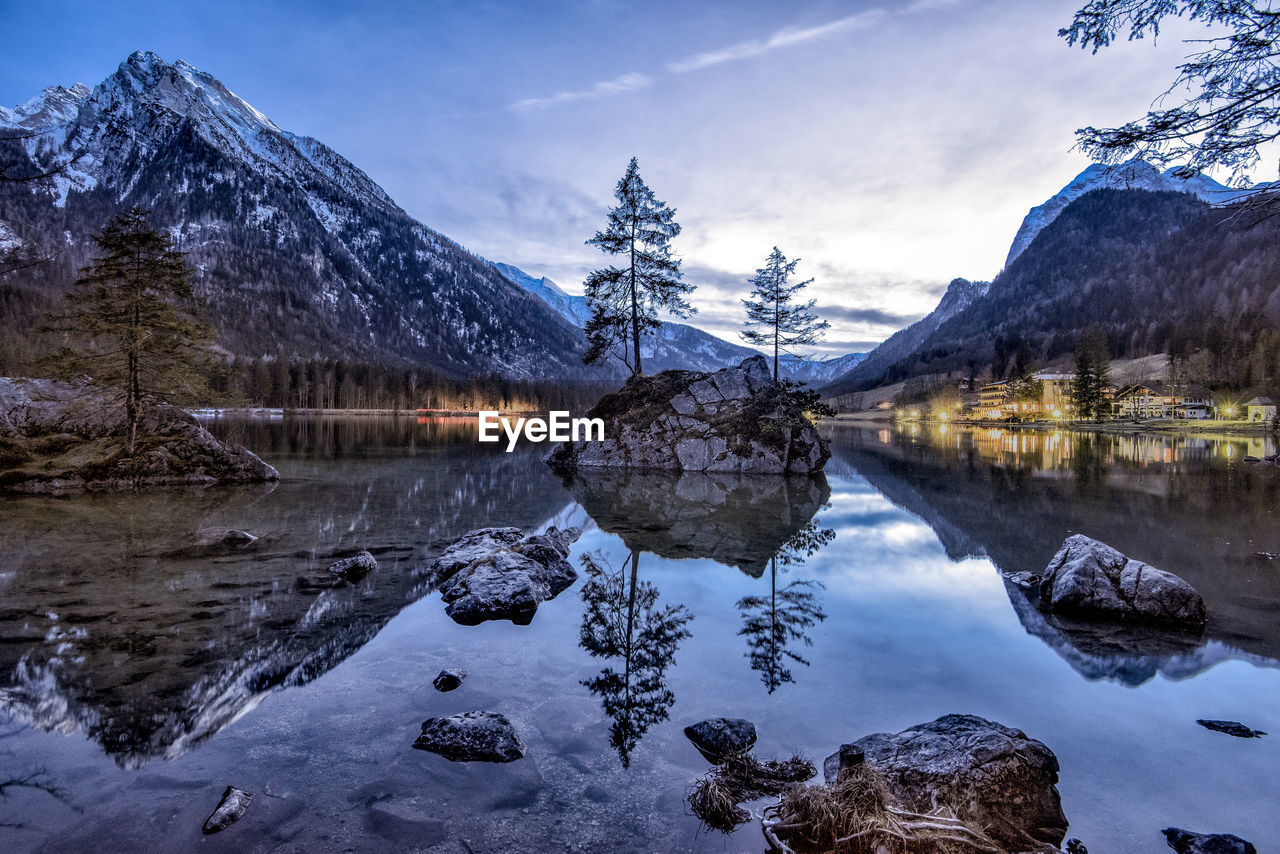 Scenic view of calm lake by mountain against sky during sunset