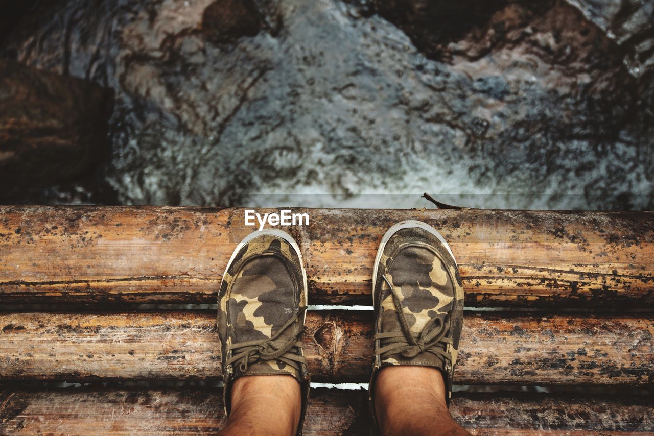 Low section of man wearing shoes while standing wooden bridge