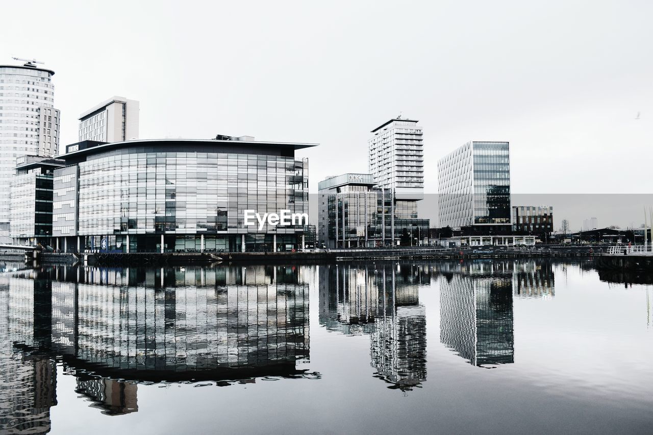 Reflection of buildings in city against clear sky