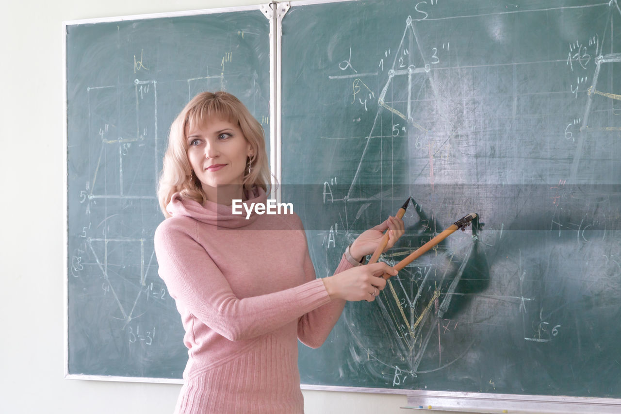 Confident teacher explaining diagram on blackboard in classroom