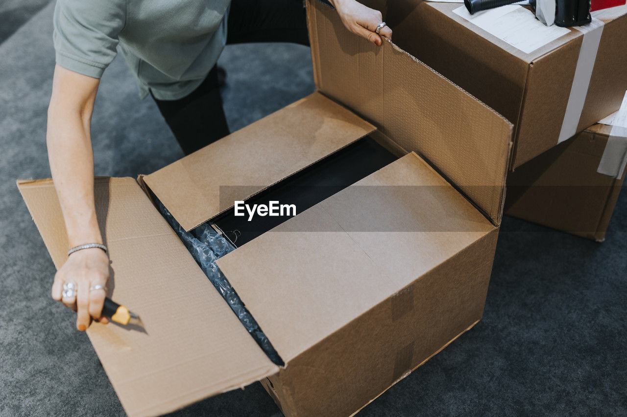 Midsection of saleswoman opening cardboard package while working in electronics store