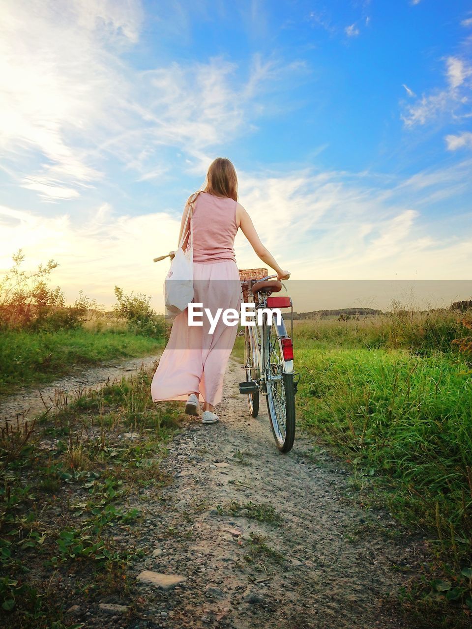Rear view of woman with bicycle walking on land against sky during sunset