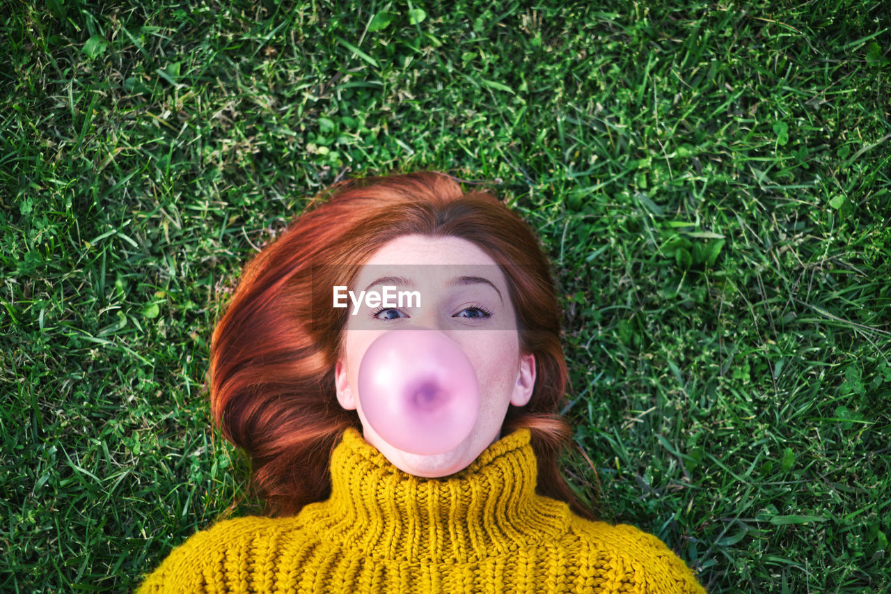 Portrait of woman blowing bubble gum while lying on grassy land