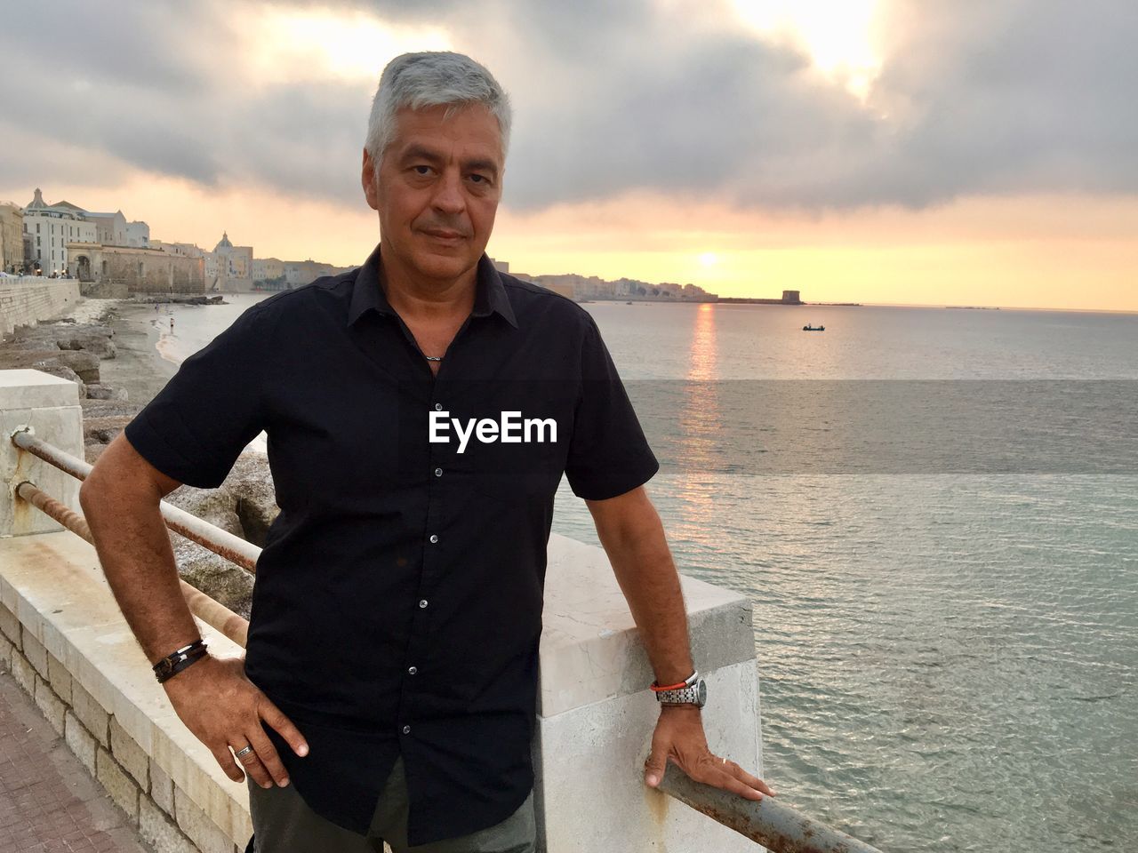 Portrait of mature man standing by railing against sky