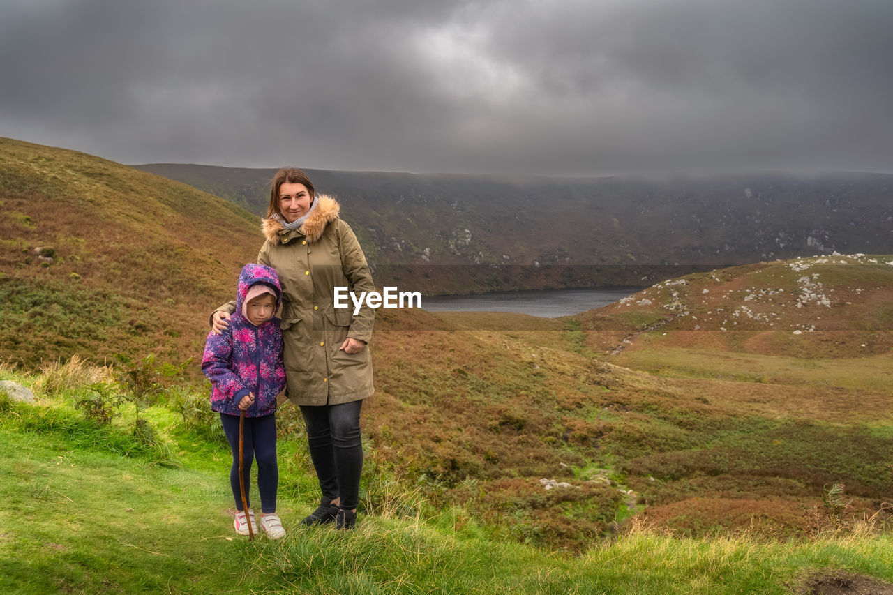 Mother and daughter standing and looking at camera, lough bray in background. wicklow mountains