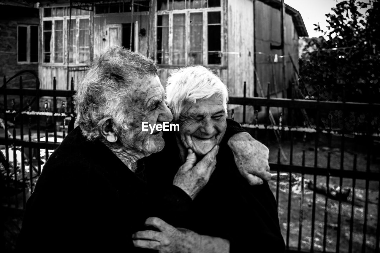 Smiling senior man embracing woman against house