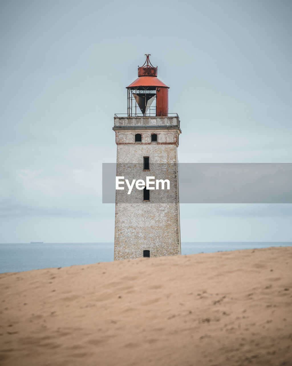 Lighthouse on beach by sea against sky